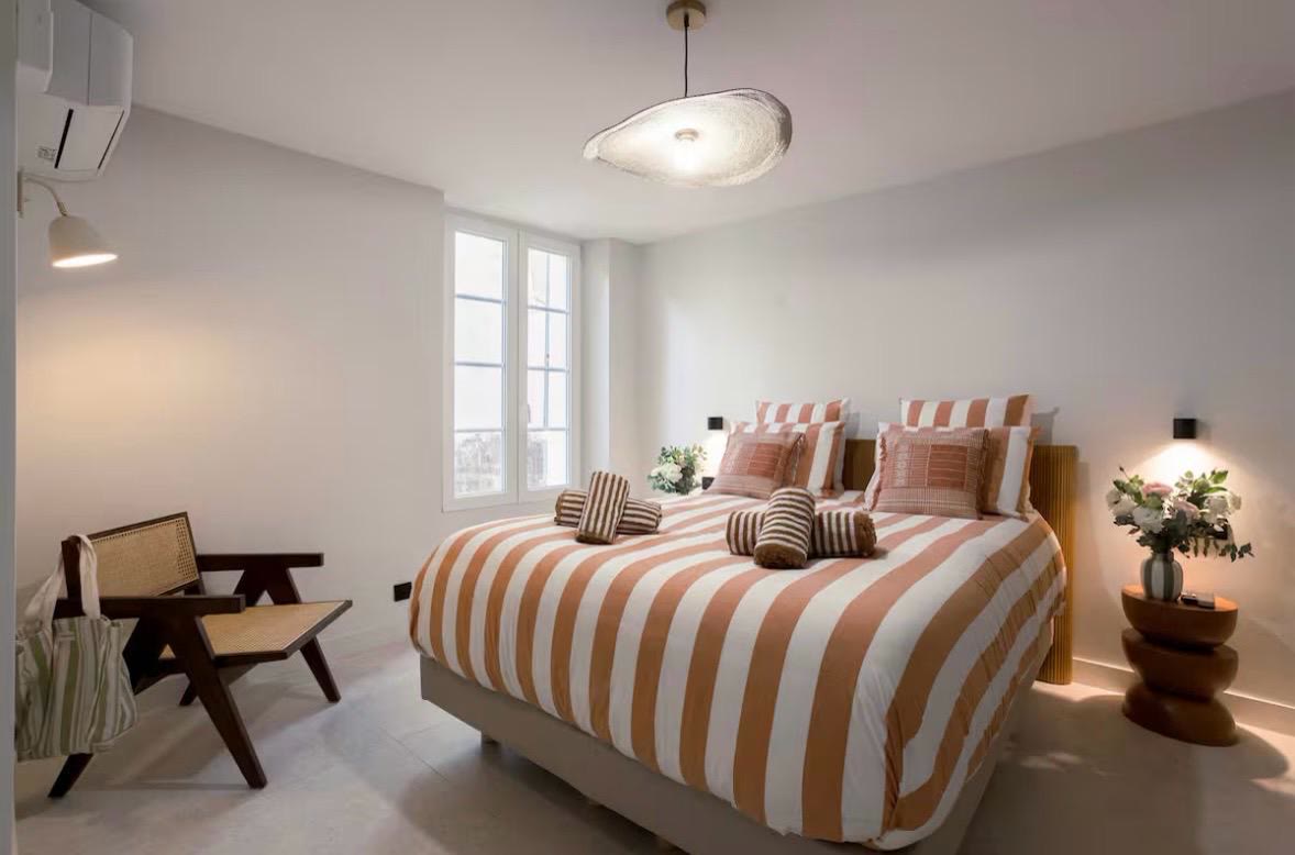 Chambre principale, tête de lit en cannage et parure aux rayures terracotta, fauteuil signature.